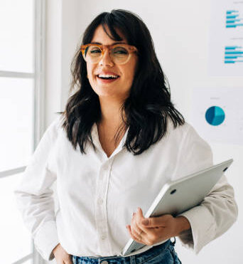 Data analyst standing in an office and looking at the camera. Portrait of a happy business woman holding a laptop in her hand.
